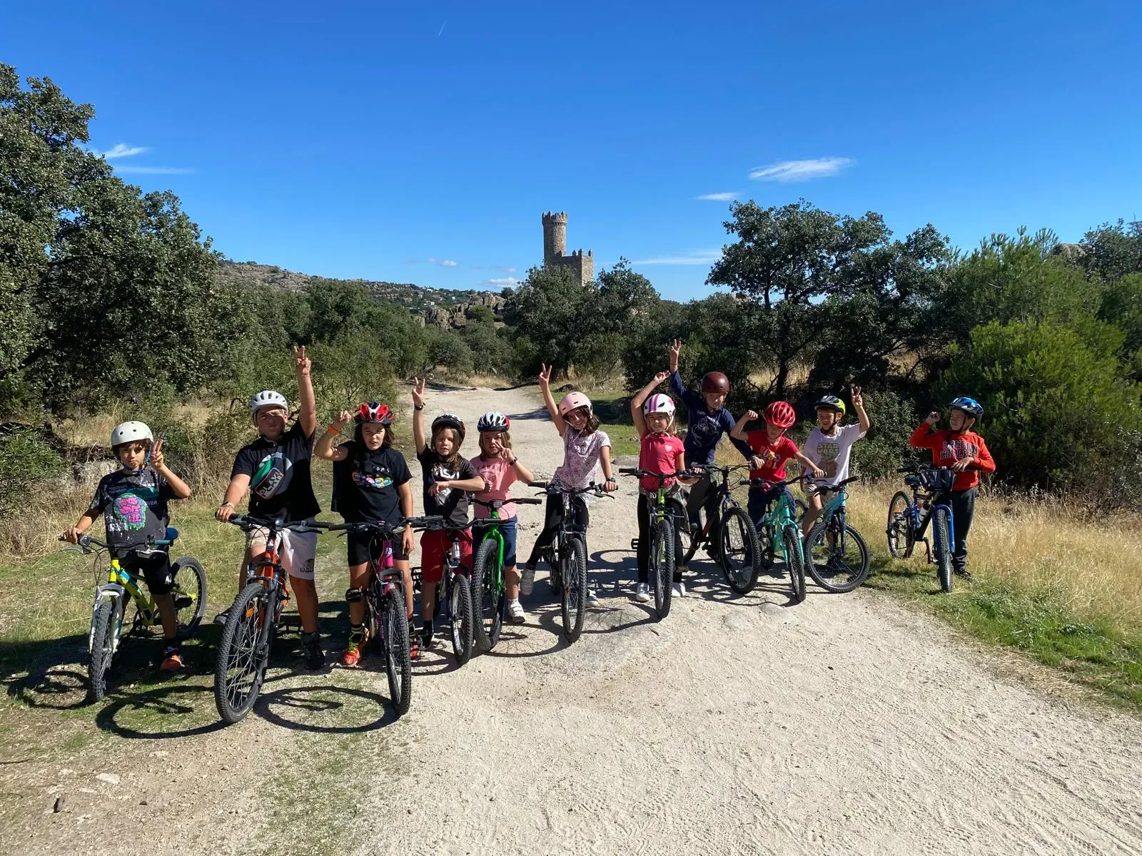 A group of students with their bicycles on a mountain track, with a tower in the distance.
