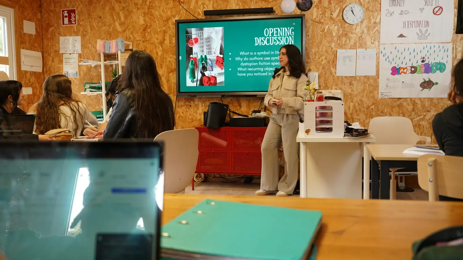 A teacher leads a class discussion in front of a screen showing the questions for the session.