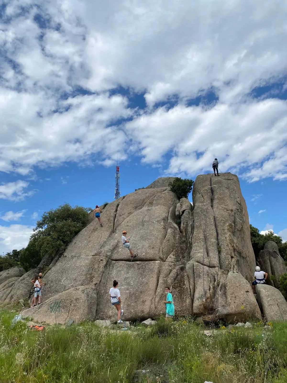 A group of students climbing a rock formation in the Sierra de Guadarrama under a clear sky.