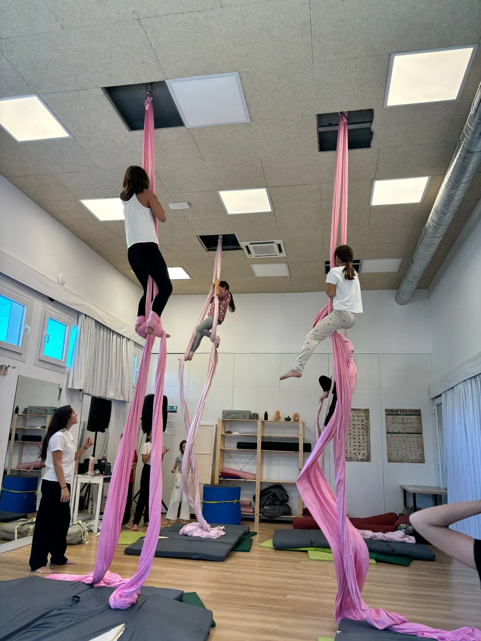 Three students practice aerial silks suspended in the school gym.