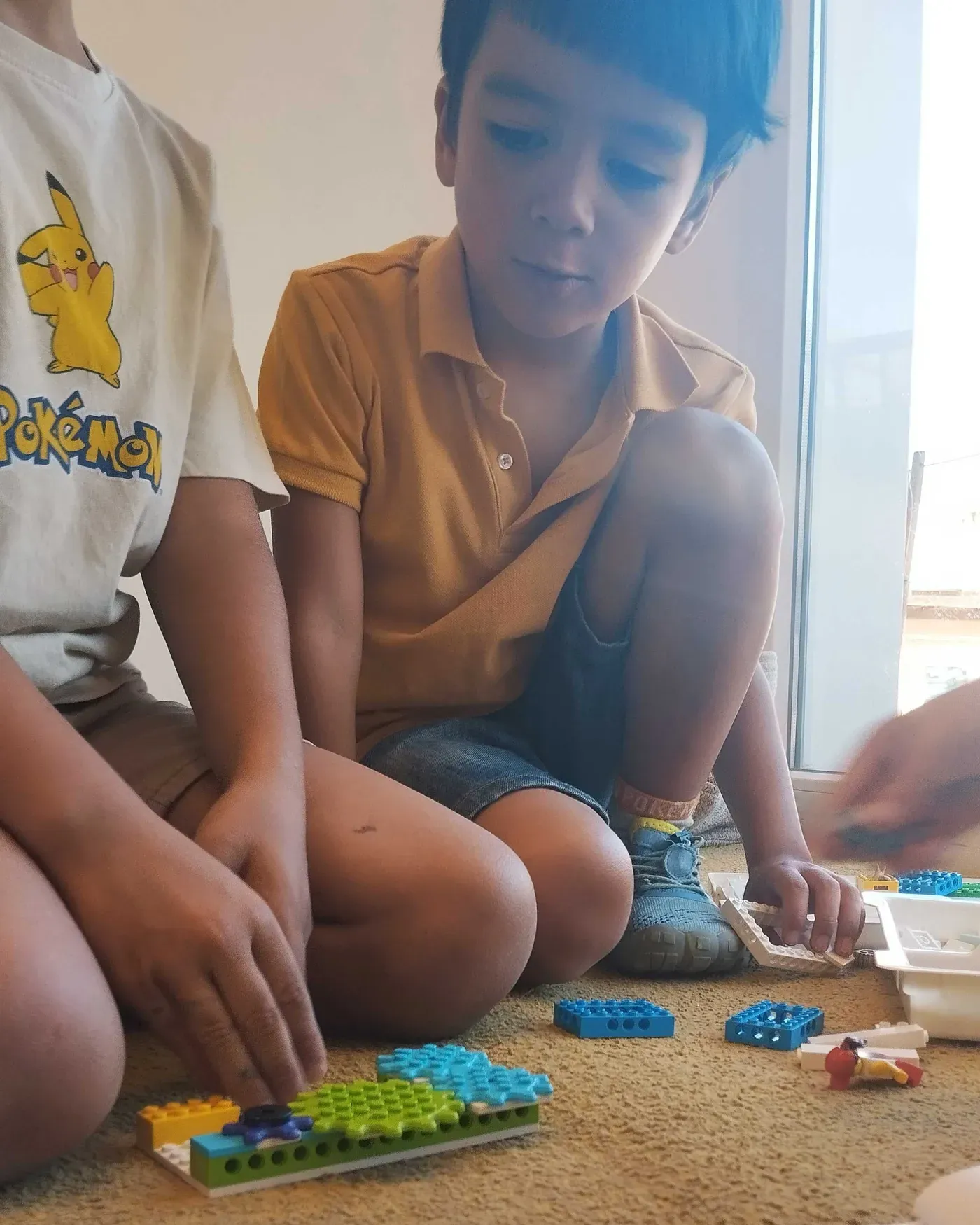 Two pupils sitting on the floor by the window put together a LEGO build