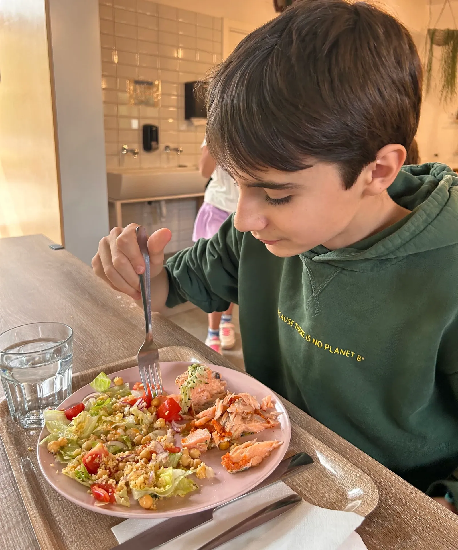 Un alumno come en el comedor un plato de ensalada con garbanzos y pescado.