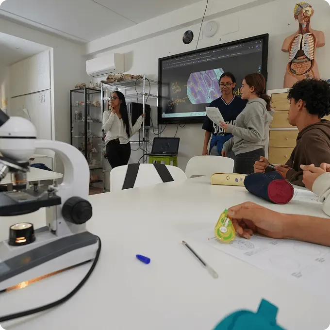 A classroom with a screen and a microscope, students working around an oval table.