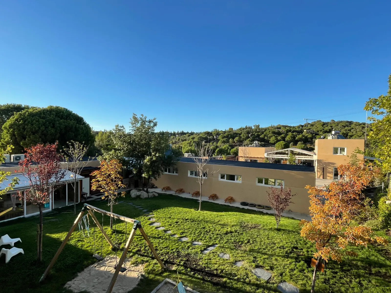 Vista del campus desde arriba: el edificio, el jardín con juegos de madera y la sierra al fondo.
