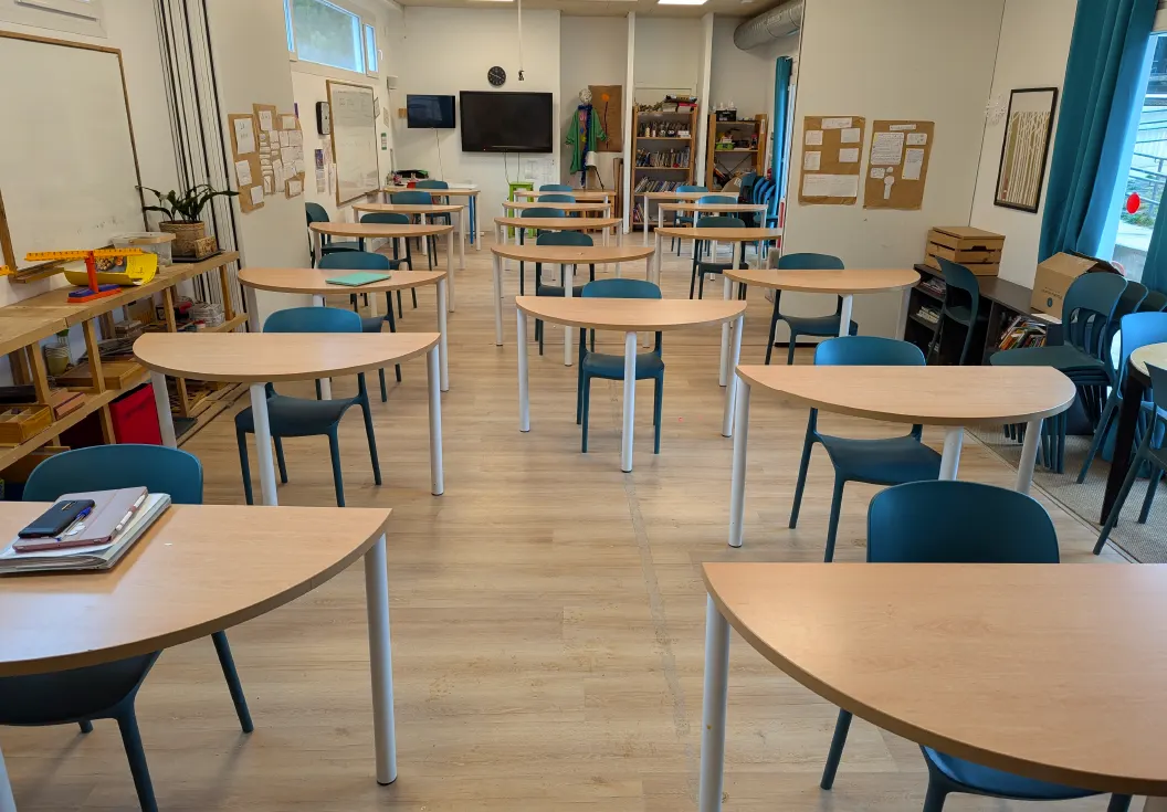 Un aula luminosa con mesas redondas y sillas azules, vacía.