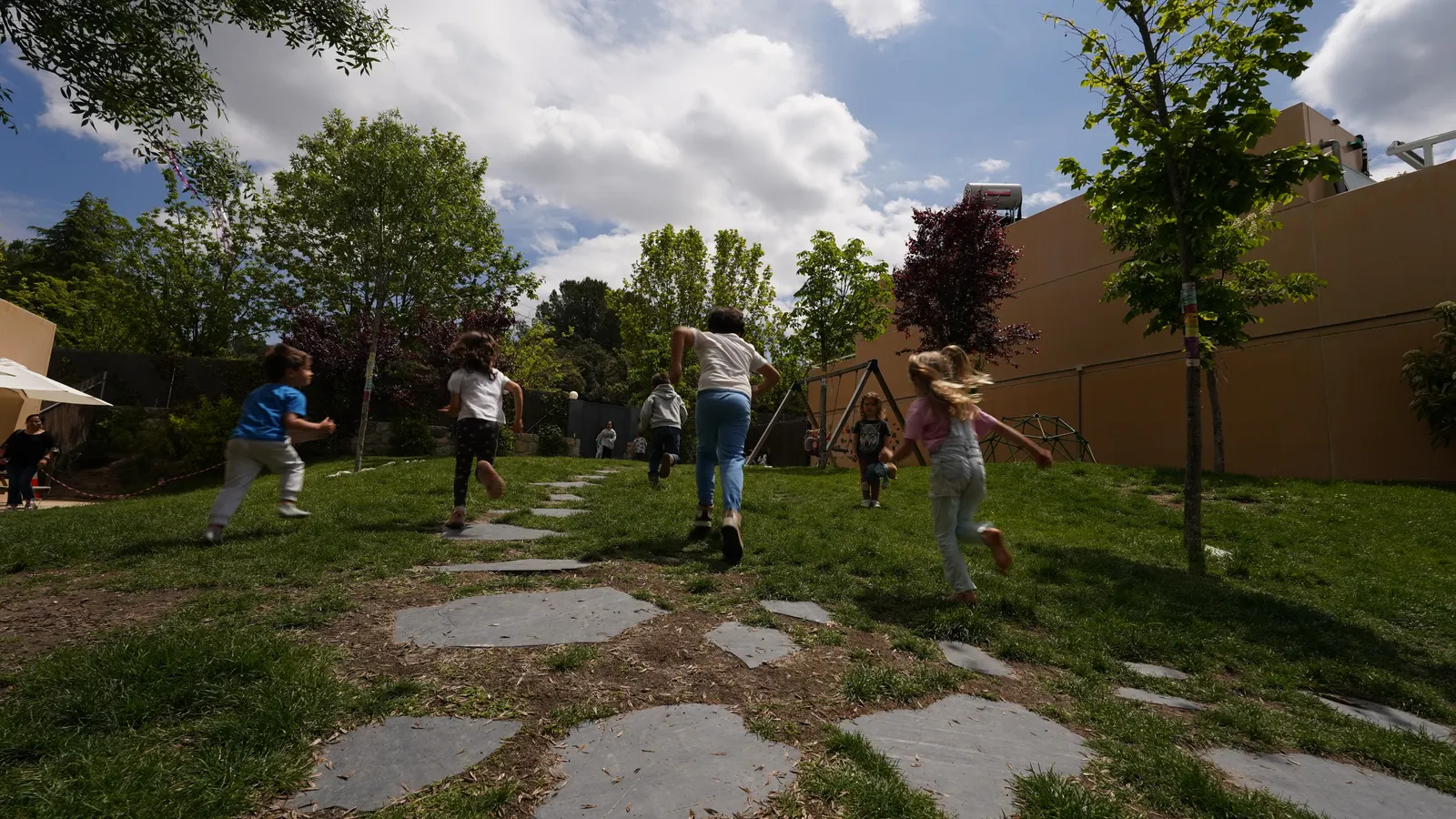 Niños corriendo por el jardín del colegio con palos de madera en la mano.