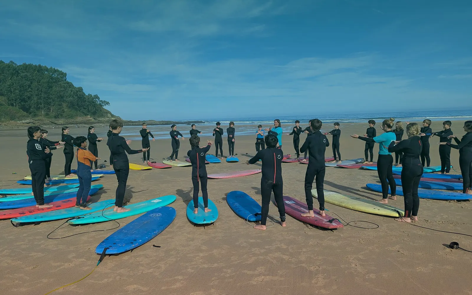 Un grupo de alumnos con traje de neopreno, de pie junto a sus tablas en la playa.