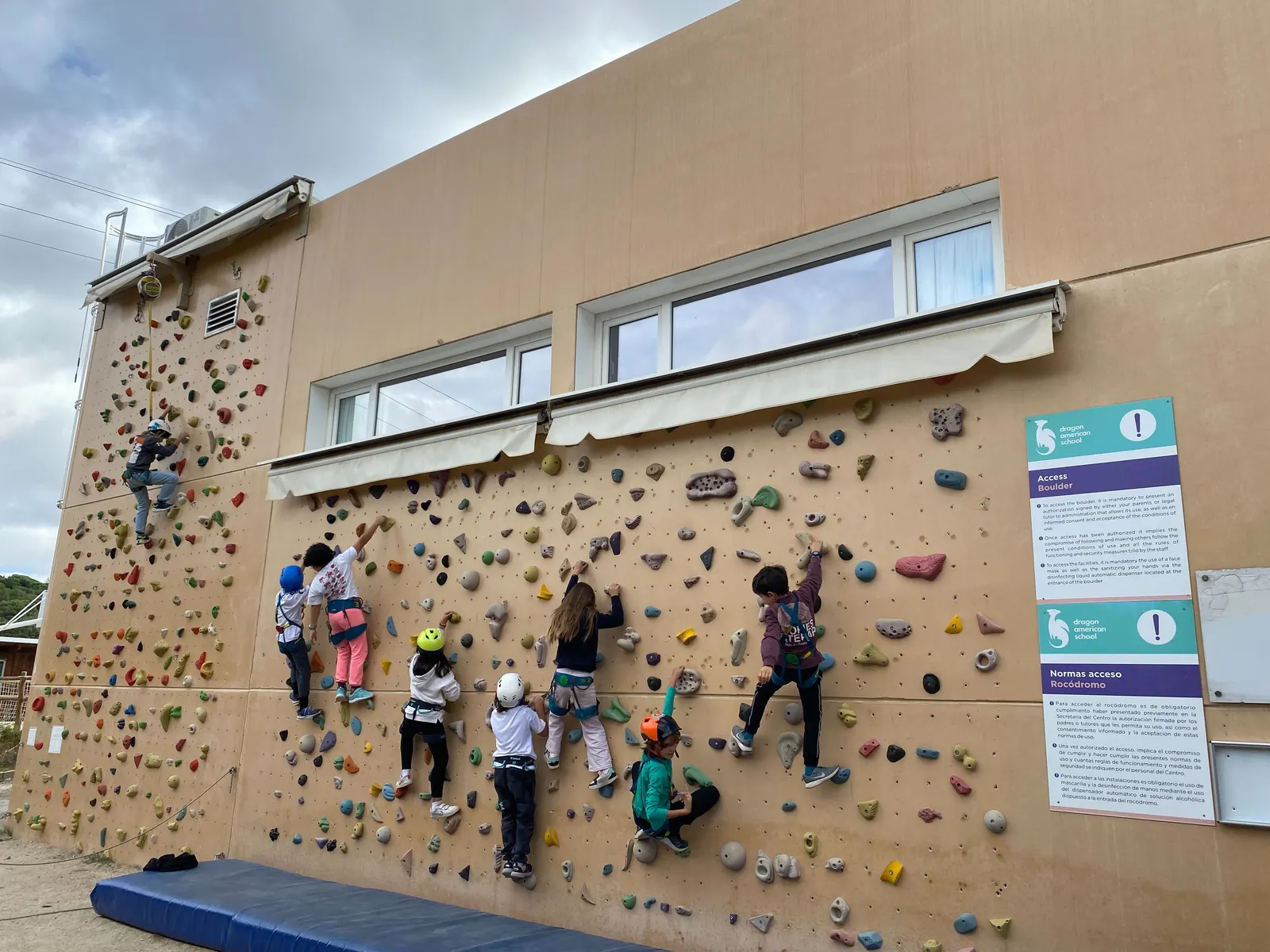 Niños escalando el rocódromo exterior del colegio, al aire libre.